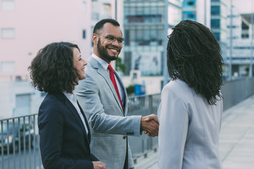 Cheerful satisfied partners finishing up meeting outside. Business man and women standing in city street, shaking hands, smiling and talking. Deal concept