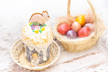 Easter holiday. Colored eggs in a basket. Easter gingerbread bunny on the sandwich. on a light wooden background.