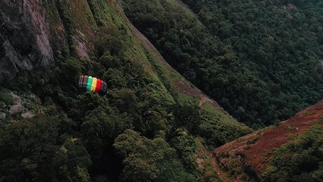 Aerial View Of Parachuter Gliding Down Through Valley And Over Lush Green Forest