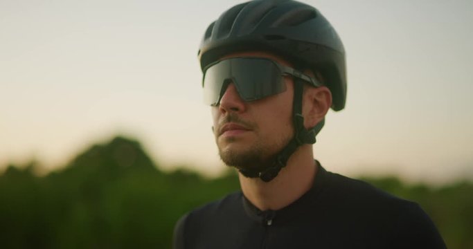 Road cyclist puts sunglasses on preparing to ride at sunset