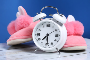 Pink girl slippers with white retro alarm clock on a wooden floor and blue background