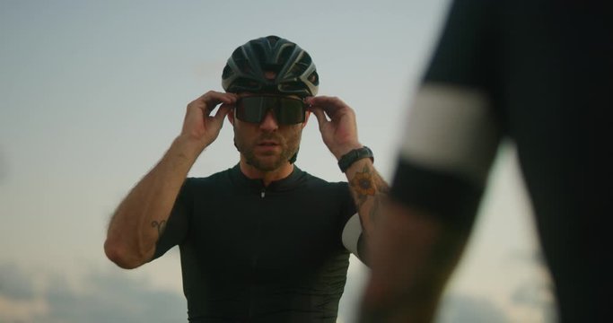 Road cyclist puts sunglasses on preparing to ride at sunset