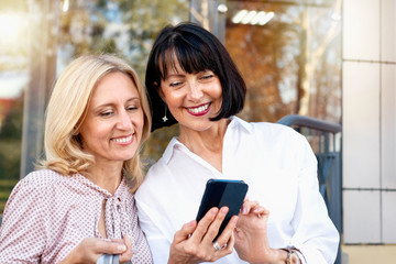Two mature women looking at the phone and having fun while doing shopping