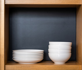 Wooden kitchen cabinet cupboard with many white and clean ceramic dishes, plates, all neatly cleaned up on shelves of modern home interior