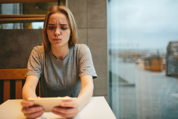 The blonde uses the phone. Girl and smartphone. A woman is sitting in a cafe with a cellular