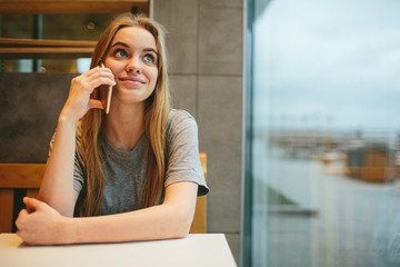 The blonde uses the phone. Girl and smartphone. A woman is sitting in a cafe with a cellular