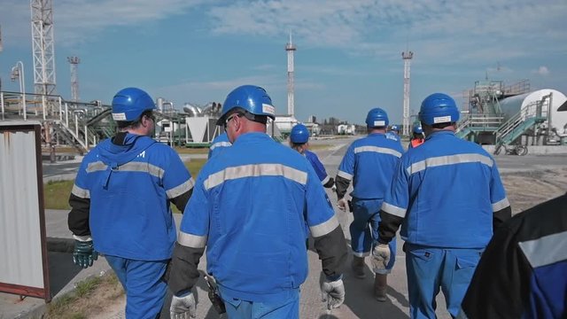 A delegation of engineers at the production site. Workers in blue overalls and helmets. Check at the oil company. A tour of the factory outdoors.