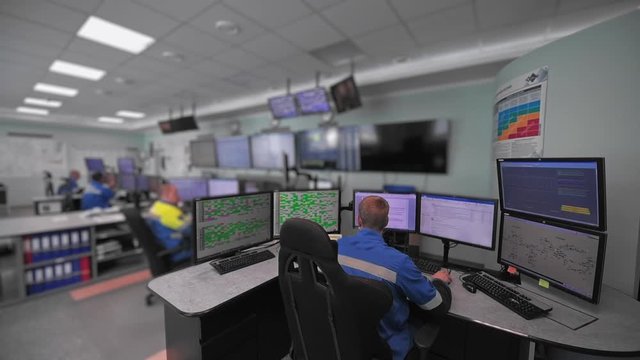 A worker sits in front of many monitors. Production room. Monitoring of technical processes in oil production. Instruments for monitoring indicators in the manufactory. Remote control.