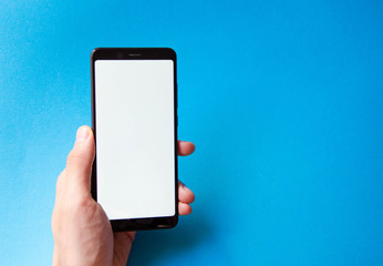 A male hand holds a smartphone, points a finger, types. Communication on a smartphone, correspondence. Place for text. Smartphone in hand on a blue  background.