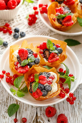 Phyllo pastry fruit cups with whipped cream filling topped with mix fresh berries sprinkled with powder sugar on a white plate top view. Delicious filo pastry dessert