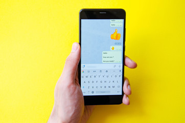 A male hand holds a smartphone, points a finger, types. Communication on a smartphone, correspondence. Place for text. Smartphone in hand on a yellow  background.