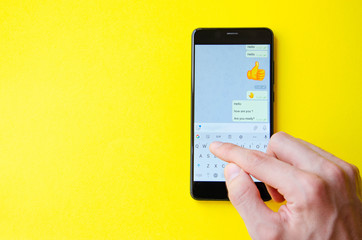 A male hand holds a smartphone, points a finger, types. Communication on a smartphone, correspondence. Place for text. Smartphone in hand on a yellow  background.
