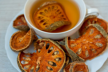 White cup of tea, made from apple-quince, standing on a white plate surrounded by dried slices of apple-quince. Closeup top view