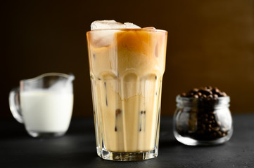 Glass of iced coffee, cream on a black table, brown background. Copy space, horizontal orientation.