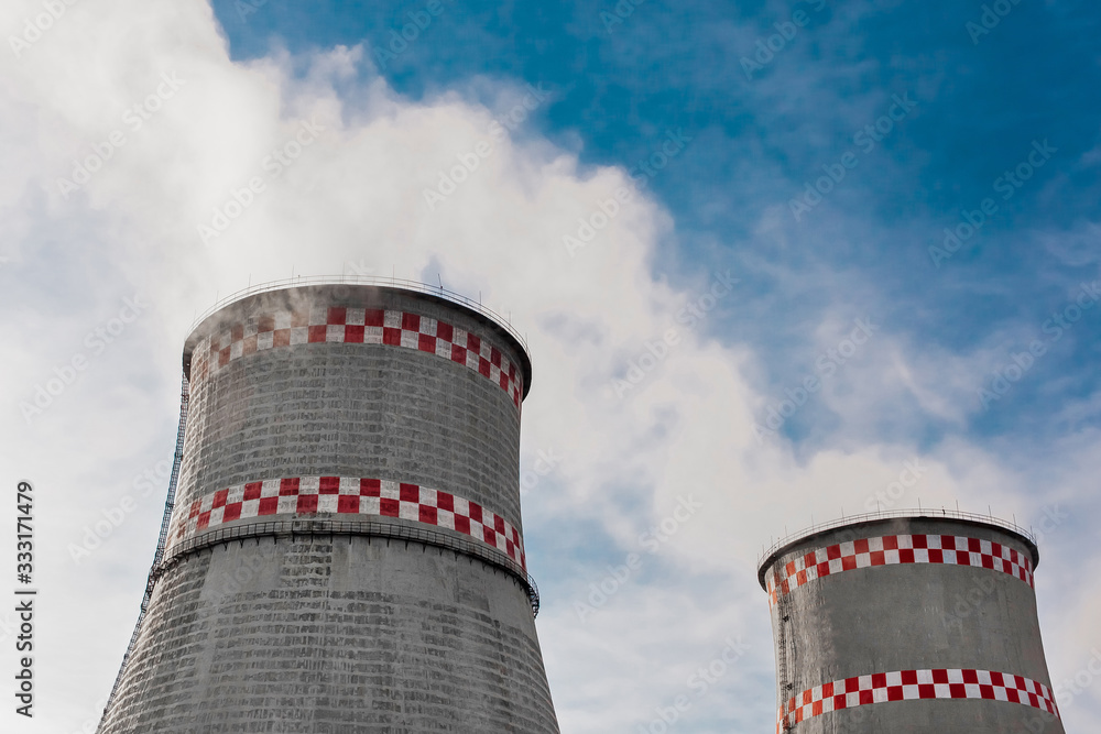 Wall mural Cooling tower, desuperheater, smoke from a pipe of an industrial plant or thermal power plant on a background of blue sky with clouds	