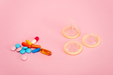 Close up view of condoms and birth control pills on pink background