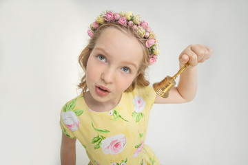 Young schoolgirl rings a golden bell on a white background in a yellow dress and with a beautiful whisk on her head of flowers