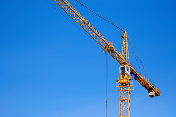 Construction crane against blue sky background. Yellow hoisting crane. Industrial construction. Copy space