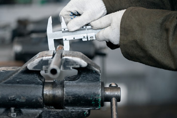Worker is taking a measurement of pipe workpiece by caliper.