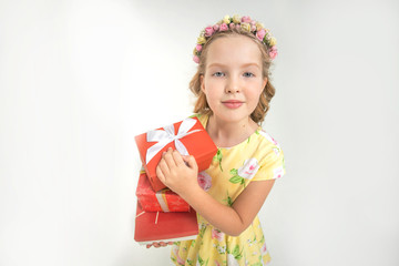 Happy little blond baby girl holding three boxes with gifts on light isolated background. Concept of celebrating, giving and receiving a gift, festively dressed girl in a dress and with a ha hairstyle