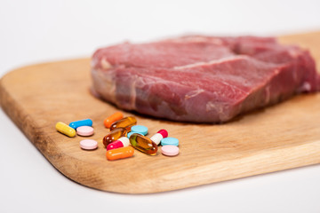 Selective focus of hormonal pills and raw meat on wooden cutting board isolated on white
