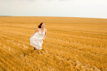 Runs across the field. Young beautiful redhead woman in the middle of a wheat field having fun. Summer landscape, good weather. Windy day with the sun and clouds. White cotton dress, eco style.