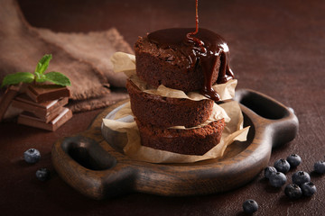 Desserts. Chocolate brownie with blueberries and mint on a brown wooden board on a brown background. The parchment between the chocolate cakes. Background image, copy space
