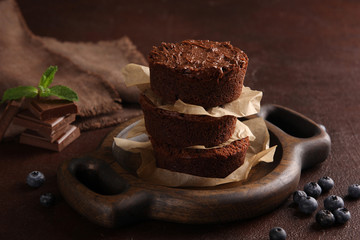 Desserts. Chocolate brownie with blueberries and mint on a brown wooden board on a brown background. The parchment between the chocolate cakes. Background image, copy space