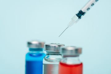 Selective focus of jars of hormonal drugs and syringe isolated on blue
