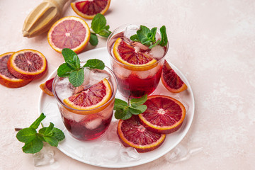 red blood orange cocktail with ice and fresh mint, top view, pink  background