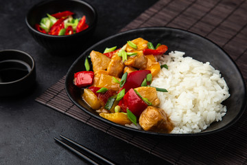 Sweet ad sour chicken served with steamed rice in black bowl