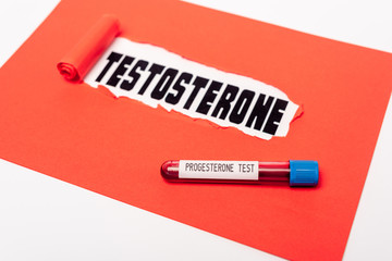 Close up view of test tube with progesterone blood sample near red paper with testosterone lettering isolated on white