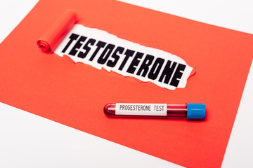 Close up view of test tube with progesterone blood sample near red paper with testosterone...