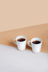 A pair of mugs with black coffee on a gray-brown geometric background. Top view