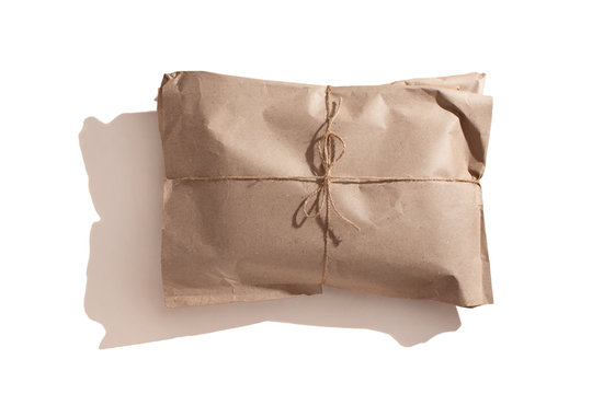 The parcel is wrapped with kraft paper and tied with a rope. Recyclable packaging material, handmade wrapper. Isolated on white background