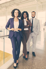 Happy confident workgroup posing for camera in contemporary office hallway. Business man and women standing together, looking at camera, smiling. Successful creative group concept