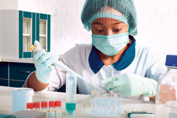 PCR test for coronavirus. African young female tech, scientist or medic in white coat and hat...