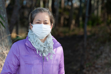 Beautiful mixed race middle aged woman wearing a white mask for protection against Coronavirus COVID-19 (SARS-CoV-2) and other contagious diseases. Front view. Copy space.