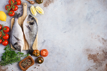 Fish dishes cooking preparation with dorado in backing form in shape of fish with healthy vegetables on gray background with ingredients, top view