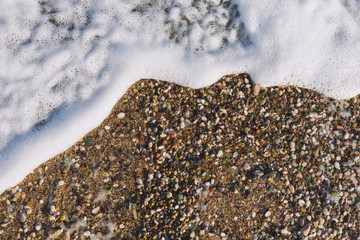 Closeup top view flatlay photography of wet brown sand of sea beach and white soft foamy tranquil wave splashing on it. Organic natural photo frame with copyspace.