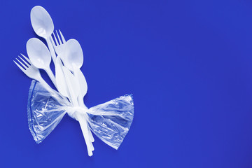 Bouquet from white disposable spoons, forks, knives on blue background close-up - Environmental problem concept