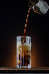Iced coffee wWIth fresh arabica espresso. FResh milk and coffee splashing into a glass filled with ice. Barista coffee with dark background