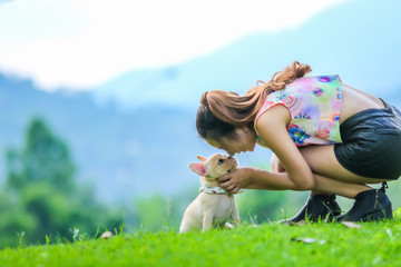 Asian young woman playing with french bulldog on green yard.