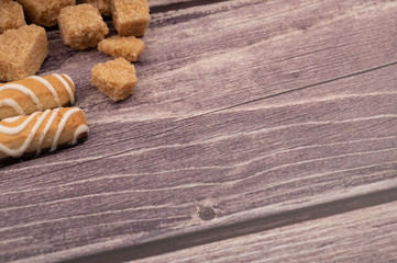 Pieces of brown cane sugar and cookie sticks with chocolate and white icing on a wooden background....
