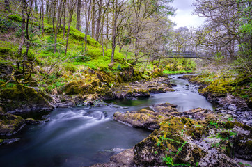 A calm image  showing a foot bridge over the River Brathay passing from Elterwater and flowing down to Skelwith in the Langdale Fells North of England.  