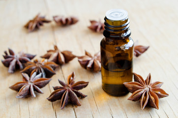 Fototapeta na wymiar Small bottle with star anise essential oil. Aromatherapy, herbal medicine and spa ingredients. Wooden background. Copy space.