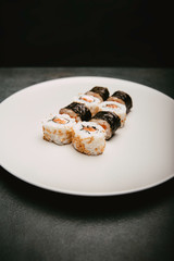 Stock photo of sushi maki, uramaki, futomaki in white plate, on black natural slab background.