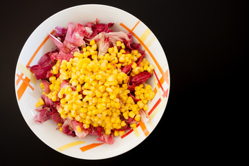 Salad with corn on black table, top view