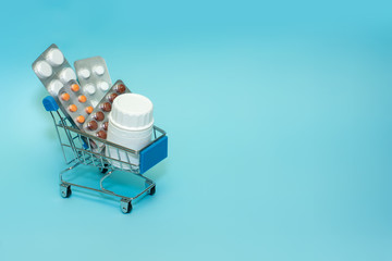 Shopping cart with pills on a blue background . The concept of the medicine of online shopping. Copy space for text