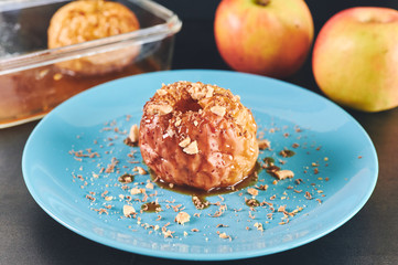 Detail of roasted apple decorated with almonds and striped chocolate on a blue plate with some apples in the background